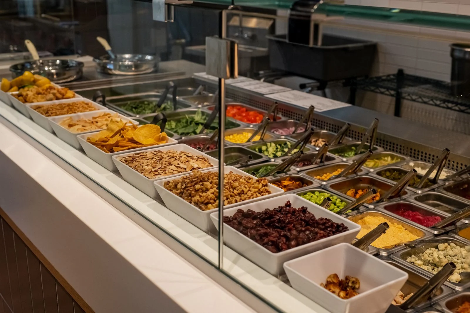 Buffet de restaurante self-service com cubas de alimentos, saladas e utensílios para servir